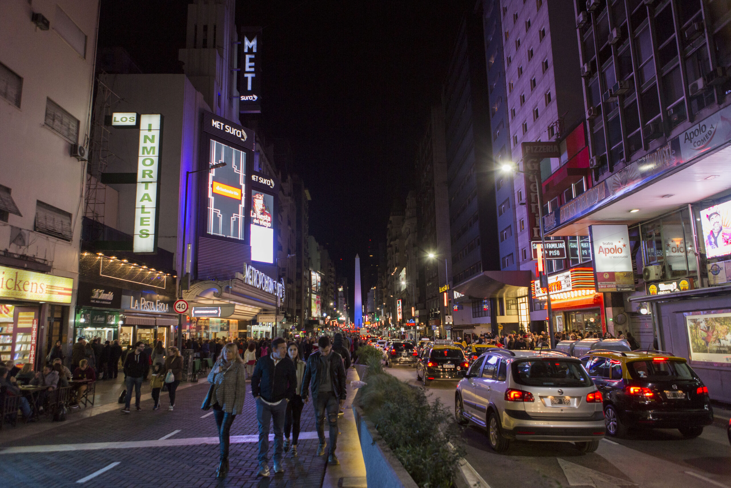 Noche de Calle Corrientes con gente caminando por la calle hecha peatonal, de fondo el obelisco iluminado de menara muy atractiva, Ciudad de Buenos Aires